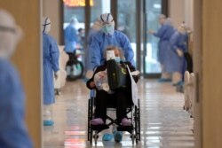 FILE - A medical worker in a protective suit moves a coronavirus patient in a wheelchair at a hospital in Wuhan, Hubei province, China, Feb. 10, 2020.