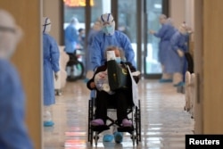 A medical worker in a protective suit moves a coronavirus patient in a wheelchair at a hospital in Wuhan, Hubei province, China, Feb. 10, 2020.
