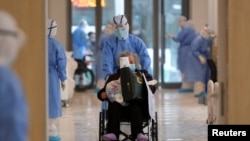 FILE - A medical worker in a protective suit moves a coronavirus patient in a wheelchair at a hospital in Wuhan, Hubei province, China, Feb. 10, 2020.