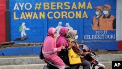 Perempuan muslim mengendarai motor di depan mural bertema virus corona di Jakarta (dok: AP)