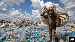 FILE — A man walks on a mountain of plastic bottles as he carries a sack of them to be sold for recycling after weighing them at the dump in the Dandora slum of Nairobi, Kenya on December 5, 2018