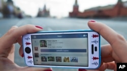FILE - A user of Russia’s leading social network internet site VKontakte, poses holding an iPhone showing the account page of Pavel Durov, the former CEO and founder of VKontakte, in Red Square in Moscow, Apr. 23, 2014. Berlin-based Telegram, created two years ago by the founder of Vkontakte, is racing to shut down broadcast channels used by Islamic State to promote its causes and recruit members. 