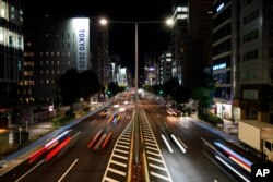 This long exposure photo shows streaks of lights from cars passing by a Tokyo 2020 Olympics and Paralympics sign on the side of a building, June 11, 2021, in Tokyo.