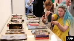 Відвідувачі "Книжкового арсеналу" фотографують книги, пошкоджені внаслідок російського обстрілу друкарні у Харкові у 2024 році. Фото: Anatolii Stepanov /AFP