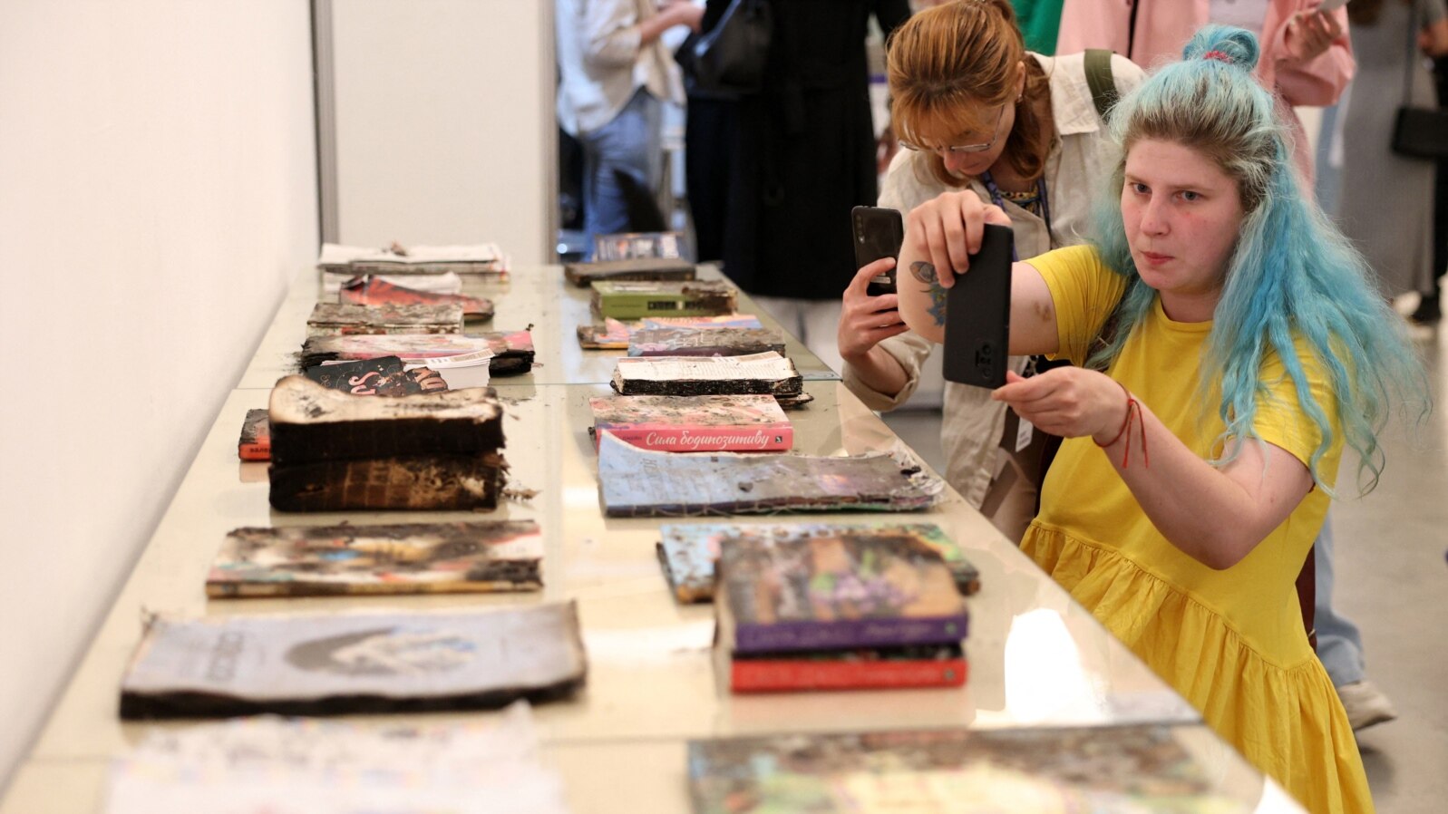 Visitors take pictures of damaged books of the Kharkiv publishing house, which were destroyed by Russian shelling on May 23, during the opening of the annual publisher's forum "Book Arsenal" in Kyiv, on May 30, 2024, amid the Russian invasion in Ukraine. 