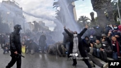  A Tunisian demonstrator flashes the V for victory sign as police fire water cannons during protests against President Kais Saied, on the 11th anniversary of the Tunisian revolution in the capital Tunis on January 14, 2022. 
