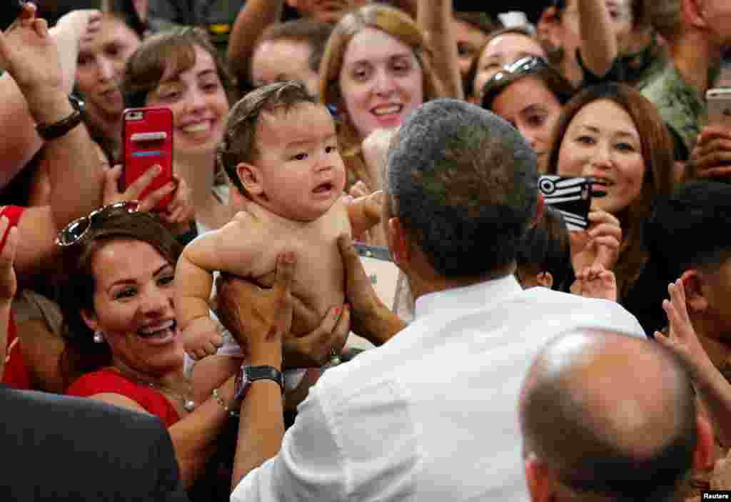 Presiden AS Barack Obama menggendong bayi dalam kunjungannya ke Stasiun Udara Korps Marinir Iwakuni dalam perjalanan menuju Hiroshima (27/5). (Reuters/Carlos Barria)
