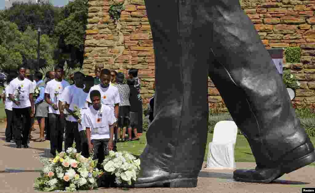 Para siswa \ meletakkan karangan bunga saat upacara resmi peringatan menandai ulang tahun pertama wafatnya mantan Presiden Afrika Selatan Nelson Mandela, di Patung Mandela terbesar di dunia di Union Buildings, Pretoria. &nbsp;