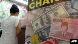 US dollar, Indonesian rupiah and Chinese renminbi currencies are displayed in the poster of a money exchange shop in Jakarta on June 12, 2013.