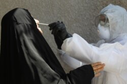 FILE - An Iraqi public hospital doctor takes samples from Iraqi citizens in Baghdad's suburb of Sadr City, April 2, 2020, as part of precautions taken by Iraq against the spread of the novel coronavirus.