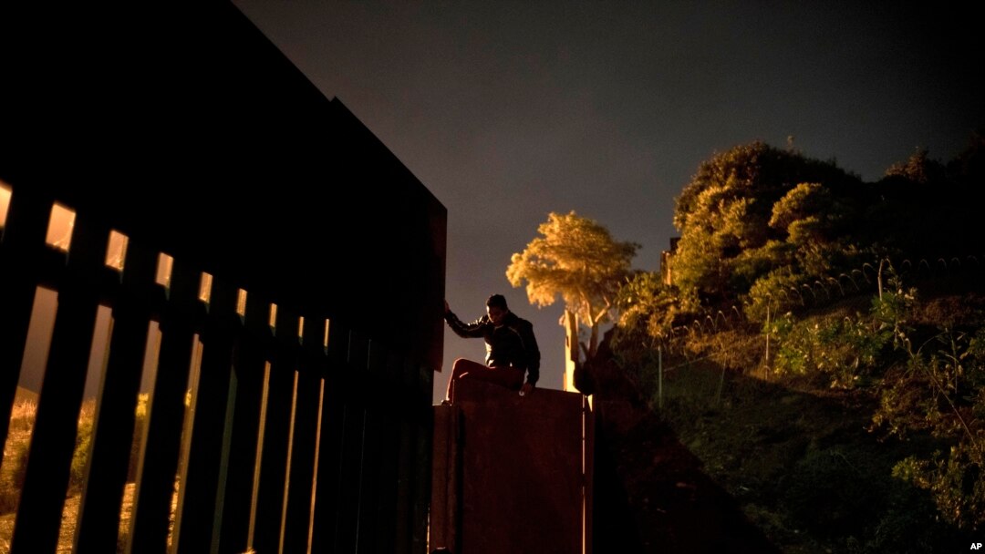 A Honduran migrant climbs the border wall separating Tijuana, Mexico and San Diego, before crossing to the U.S with his son in Tijuana, Mexico, Nov. 29, 2018. 