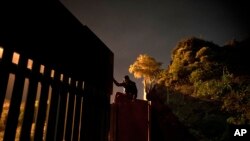 A Honduran migrant climbs the border wall separating Tijuana, Mexico and San Diego, before crossing to the U.S with his son in Tijuana, Mexico, Nov. 29, 2018. 