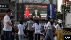 北京街头的行人观看电子屏幕上中国国家主席习近平通过视频在世卫大会视频开幕式上致辞。（2020年5月18日）