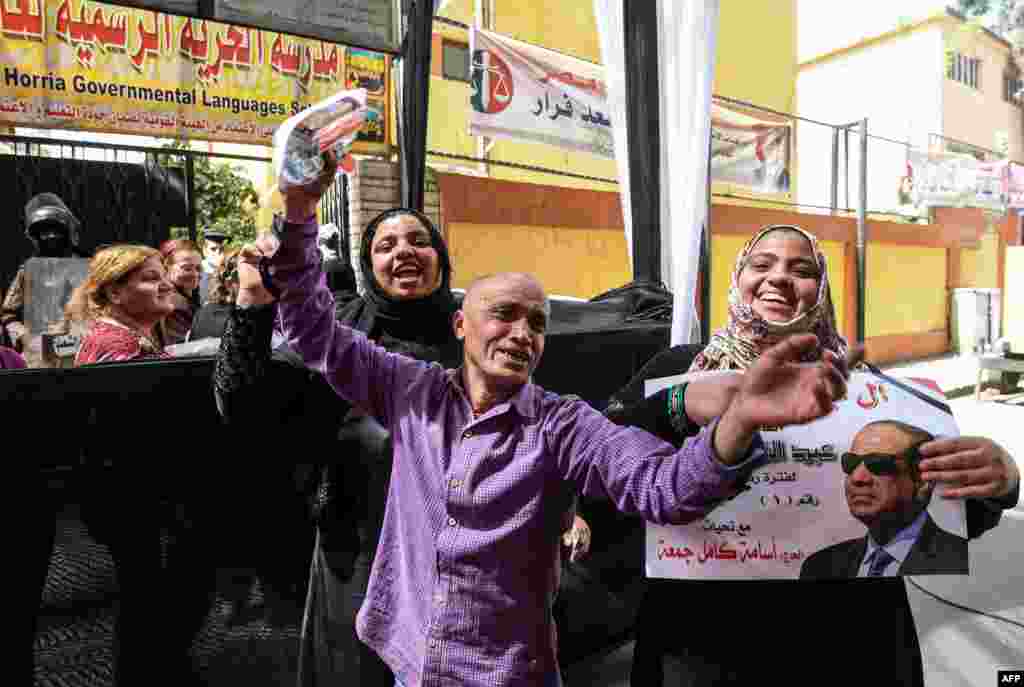 Egyptians dance and celebrate with an electoral poster of incumbent President Abdel Fattah al-Sisi outside a polling station in the capital Cairo's central neighbourhood of Abdin on the first day of voting in the 2018 presidential election.