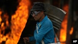 Un manifestante equipado con un escudo metálico camina frente a un autobús quemado el sábado en Caracas.