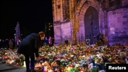 A woman bends to place a tribute with flowers and candles left near the 'Alter Markt' Christmas market, where a man drove a car into the crowd through an emergency exit route on Friday evening, in Magdeburg, Germany, Dec. 22, 2024. 