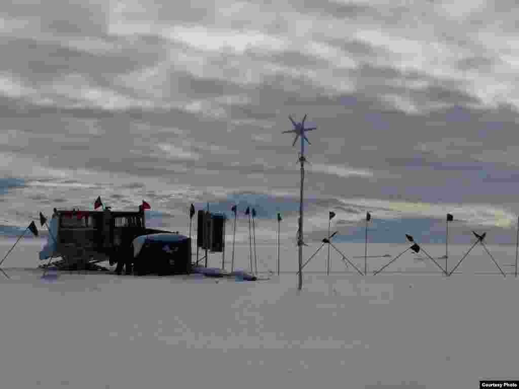 Last look at the site before winter sets in. The instrumentation package was powered by solar panels during the summer months (seen just in front of the snowcat) and an experimental wind turbine for the dark winter. The surface instruments, including daily satellite data link, consumed less than 8 watts, or about the same as a bathroom night light. (Scott Tyler) 