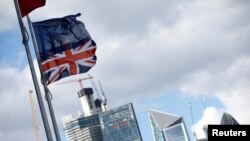 FILE - Flags flutter in the wind with the financial district in the background, in London, Sept. 23, 2018. 