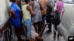 FILE— A woman lies on the pavement as she mourns a family member shot dead by unknown assailants as he sat on his motorcycle in the Delmas area of Port-au-Prince, Haiti, March 8, 2024. 