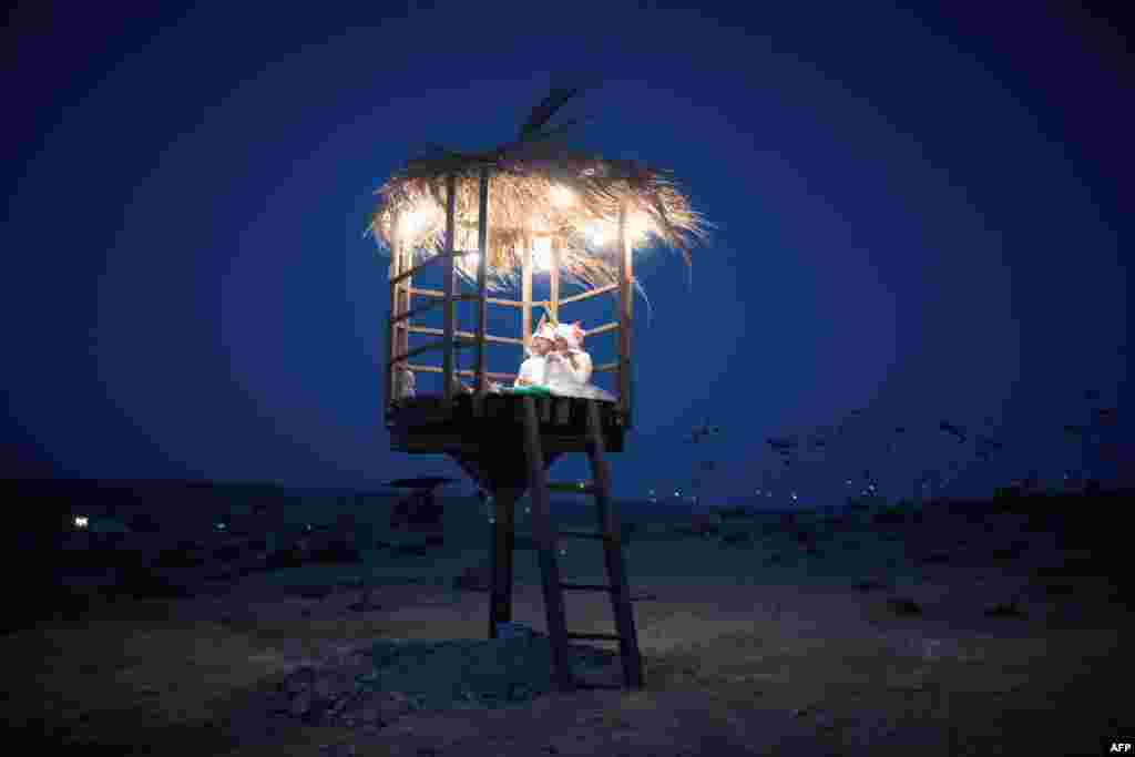 이스라엘 네게브 사막에서 열린 '2015 미드번 축제'에서 한 커플이 불을 밝힌 오두막 위에 앉아있다.