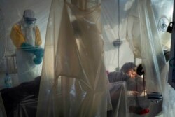 FILE - Health workers wearing protective gear check on a patient isolated in a plastic cube at an Ebola treatment center in Beni, Congo, July 13, 2019.