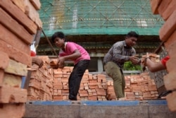 FILE - Cambodian laborers unload bricks at an under-construction luxury high-rise building complex in Phnom Penh, June 12, 2018.