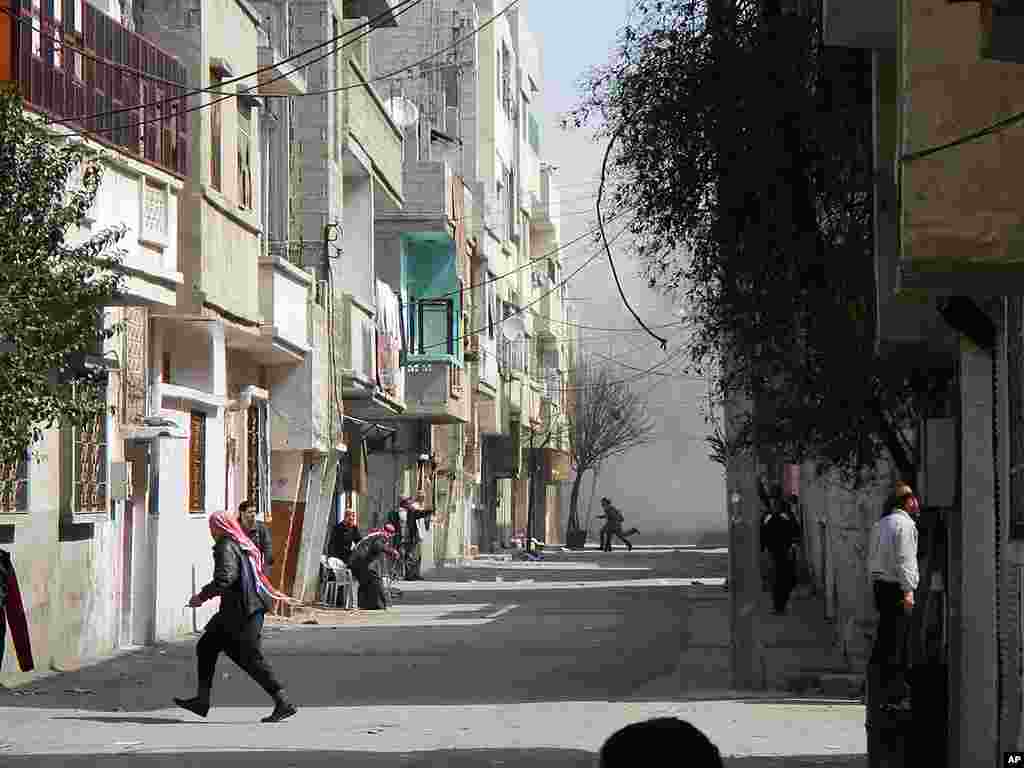 People run for cover from smoke after a shelling in the Karm al-Zeitoun area in Homs, Syria, March 12, 2012. (Reuters)