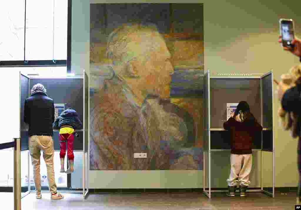 A mother uses her phone to take a picture of her husband and child in a voting booth, left, before voting a general election at the Van Gogh Museum in Amsterdam, Netherlands.