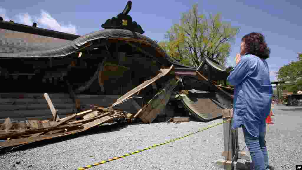 A woman prays in front of the historic Aso Shrine collapsed by powerful earthquakes in Aso, Kumamoto prefecture, April 17, 2016.