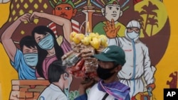 Seorang penjaja makanan melewati mural layanan masyarakat untuk mengingatkan penggunaan masker di tengah pandemi Covid-19 di Jakarta, 15 Desember 2020. (AP Photo/Tatan Syuflana)