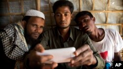 In this Jan. 14, 2018 photo, Rohingya Muslim refugee Mohammad Karim, 26, center, shows a mobile video of Gu Dar Pyin's massacre to other refugees in Kutupalong refugee camp, Bangladesh. On Sept. 9, a villager from Gu Dar Pyin, captured three videos of mass graves that were time-stamped between 10:12 a.m. and 10:14 a.m., when he said soldiers chased him away. When he fled to Bangladesh, Karim removed the memory card from his phone, wrapped it in plastic and tied it to his thigh to hide it from Myanmar police. 