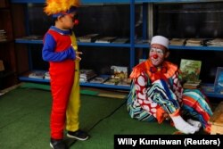 Yahya Edward Hendrawan, seorang guru berusia 38 tahun yang berpakaian seperti badut untuk mengajar, berbicara dengan putranya yang berusia 5 tahun Mirza, saat mereka bersiap untuk mengajar anak-anak selama Ramadhan, di Tangerang. (Foto: Reuters/Willy Kurniawan)