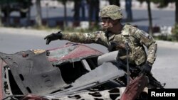 FILE - A U.S. soldier inspects the site of a suicide bomb attack in Kabul, Afghanistan, June 30, 2015. President Barack Obama has approved giving the U.S. military greater ability to accompany and enable Afghan forces in a move to assist them more proactively on the battlefield.