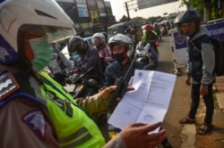 Seorang perwira polisi Indonesia memeriksa dokumen dari seorang pengendara kendaraan bermotor yang menuju ke Ibu Kota Jakarta, di Bekasi, Jawa Barat, pada tanggal 29 Mei 2020, di tengah pembatasan perjalanan selama pandemi virus coronavirus COVID-19. (Foto oleh REZAS / AFP)