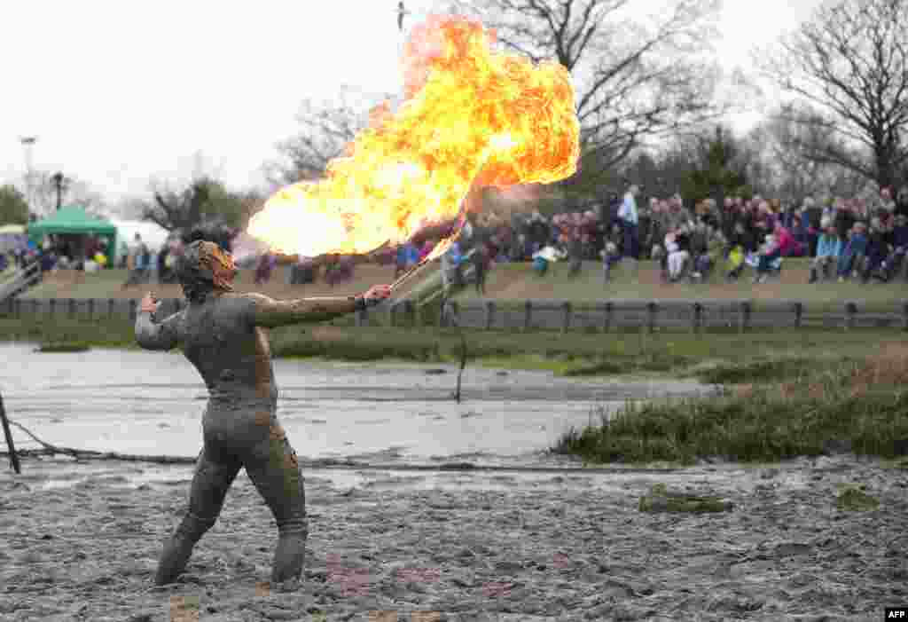 영국 말든에서 열린 진흙 달리기 대회에서 결승선을 통과한 참가자가 불을 내뿜는 묘기를 선보이며 자축하고 있다.