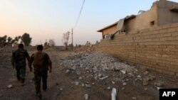 FILE - Peshmerga fighters walk past a damaged house in an Iraqi Kurdish Kakai minority village located near the town of Kalak, east of Mosul, Oct. 26, 2016.