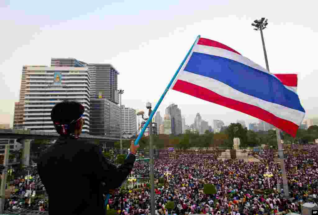 یک تظاهرکننده تایلندی پرچم ملی این کشور را طی تظاهرات در بانکوک در هوا تکان می دهند. ۲۲ دسامبر