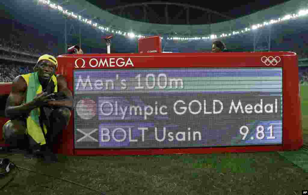 Usain Bolt de la Jamaïque pose à côté du panneau de chronométrage après avoir remporté la médaille d'or en finale de 100 mètres hommes à Rio de Janeiro, Brésil, 14 août 2016.