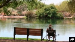 In this April 30, 2020 photo, a fisherman watches his line from the shade at Veterans Oasis Park in Chandler, Ariz. People have been turning to fishing at community lakes as a chance to go outdoors and still following social-distancing guidelines. (AP Photo/John Marshall)