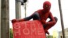 Seorang relawan mengenakan kostum Spiderman merentangkan spanduk bertuliskan anjuran agar tetap di rumah untuk mencegah penularan virus corona (COVID-19) di Makassar, Sulawesi Selatan, 17 April 2020. (Foto: Antara via Reuters)