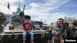 A boy sits on an armored personnel carrier (APC) as he poses for a picture during a parade in Luhansk, eastern Ukraine, September 14, 2014. Ukraine's Defence Minister said on Sunday that NATO countries were delivering weapons to his country to equip it to