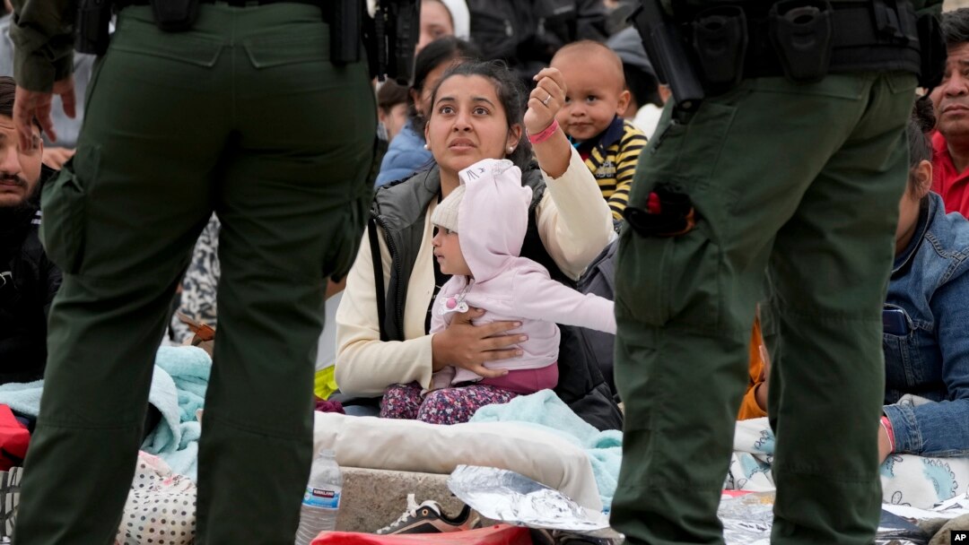 Una mujer sostiene su pulsera para mostrar a los agentes de la Patrulla Fronteriza de EEUU que ella y su hija han estado esperando más tiempo entre dos muros fronterizos para solicitar asilo, el viernes 12 de mayo de 2023, en San Diego. (Foto AP/Gregory Bull)