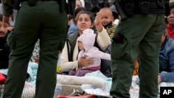 Una mujer sostiene su pulsera para mostrar a los agentes de la Patrulla Fronteriza de EEUU que ella y su hija han estado esperando más tiempo entre dos muros fronterizos para solicitar asilo, el viernes 12 de mayo de 2023, en San Diego. (Foto AP/Gregory Bull)