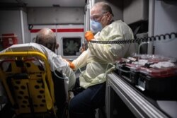 FILE - A paramedic wearing personal protection equipment (PPE) rides in an ambulance with a male patient showing COVID-19 symptoms in Stamford, Connecticut, April 4, 2020.