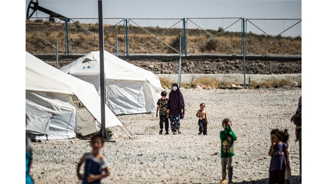 FILE - A woman clad in mask due to the COVID-19 pandemic walks next to a child by tents at Camp Roj, housing people who were relocated from al-Hol camp, in Syria's northeastern Hasakah province, Sept. 30, 2020.