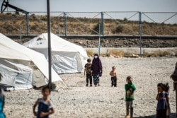 A woman clad in mask due to the COVID-19 pandemic walks next to a child by tents at Camp Roj, housing people who were relocated from al-Hol camp, in Syria's northeastern Hasakah province, Sept. 30, 2020.