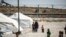 FILE - A woman clad in a mask due to the COVID-19 pandemic walks next to a child by tents at Camp Roj, housing people who were relocated from al-Hol camp, in Syria's northeastern Hasakah province, Sept. 30, 2020.