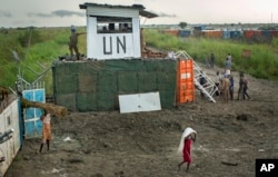 FILE - Displaced South Sudanese next to United Nations peacekeepers from Mongolia guarding the gate, at a makeshift camp at the United Nations Mission in South Sudan (UNMISS) base in the town of Bentiu, South Sudan, Sept. 22, 2014.