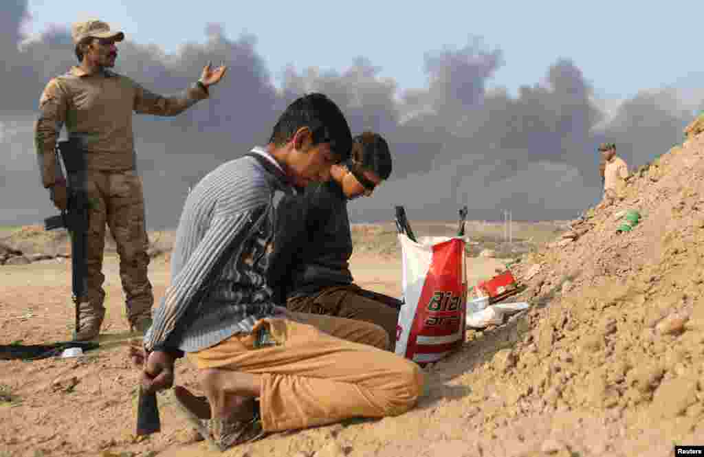 یک سرباز عراقی بالا سر دو مرد بازداشت شده، که به باور ارتش عراق، آنها جنگنده داعش هستند، ایستاده است. قیاره، عراق.&nbsp;