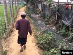 A man walks between a rice field and the shacks of Rohingya refugees living on the land of Bangladeshi farmer Jorina Katun near the Kutapalong refugee camp in the Cox's Bazar district of Bangladesh, Feb. 9, 2018.